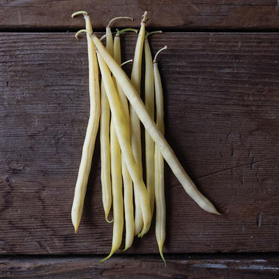 A photograph of fresh yellow wax beans on a wooden surface.