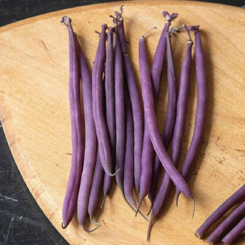 A group of purple Bean Bush Celine pods on a wooden cutting board.