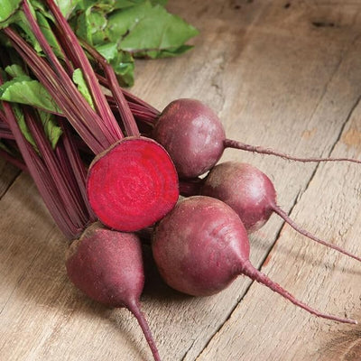 A cluster of red beet roots with green leaves on a wooden surface.