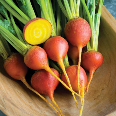 A group of golden-fleshed beet roots with green leaves and yellow stems in a wooden bowl.