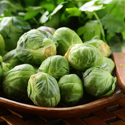 A wooden bowl filled with fresh green Brussels sprouts, with parsley leaves in the background.
