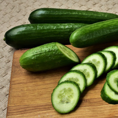 A group of fresh green cucumbers on a wooden cutting board, with some sliced pieces visible.