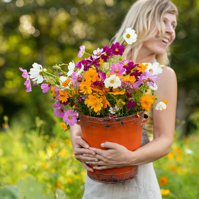 Woman holding a large pot of colorful flowers in a garden setting