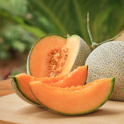 An image showing a whole cantaloupe and some slices of cantaloupe on a wooden surface, with the background blurred.