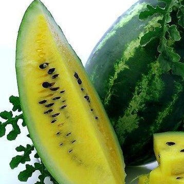 A halved yellow watermelon showing the deep yellow flesh and black seeds, with a whole watermelon and green leaves in the background.