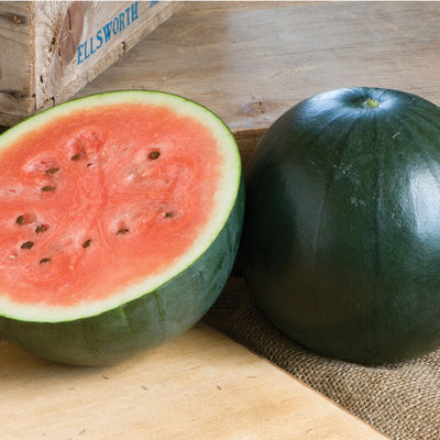 A whole Sugar Baby watermelon next to a sliced piece of the same watermelon, displaying the seed-filled interior.