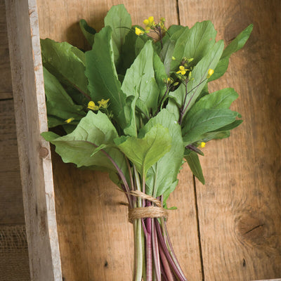 A bunch of leafy green vegetables with purple flower stems tied together on a wooden surface.