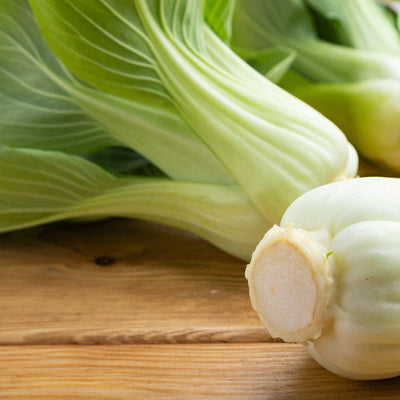 Green Pac Choi with white stems and leaves, on a wooden surface.