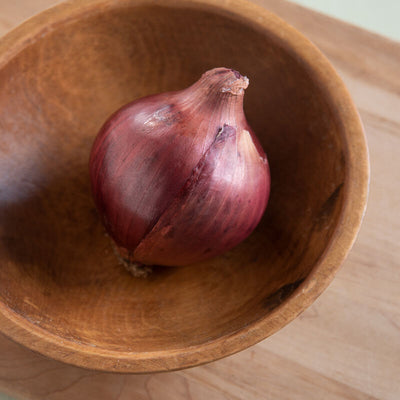 A single red onion bulb in a wooden bowl on a wooden surface.