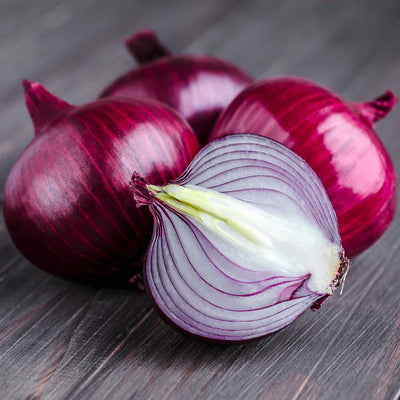 Red onions on a wooden surface with one onion sliced open.