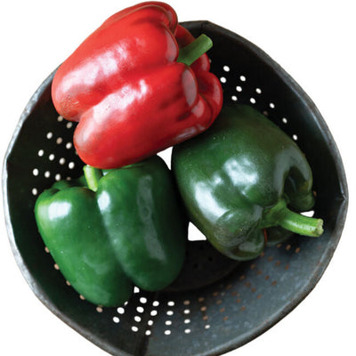 Red and green bell peppers in a black colander on a wooden surface