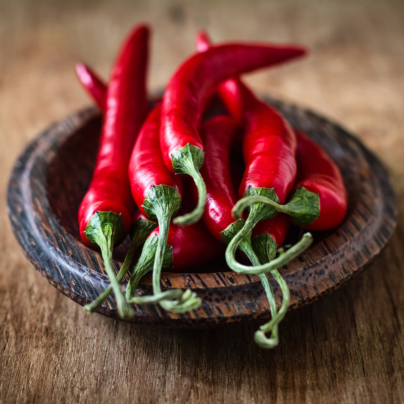 A group of fresh red Fresno chili peppers on a wooden bowl placed on a wooden surface.