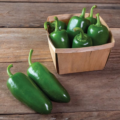 A wooden basket containing fresh green Jalapeno Pantera peppers on a wooden surface.