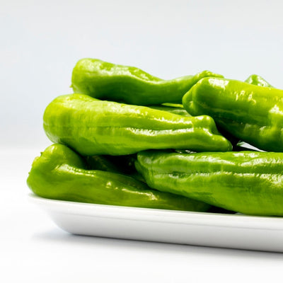 A group of fresh green Cubanelle peppers placed on a white plate against a white background.
