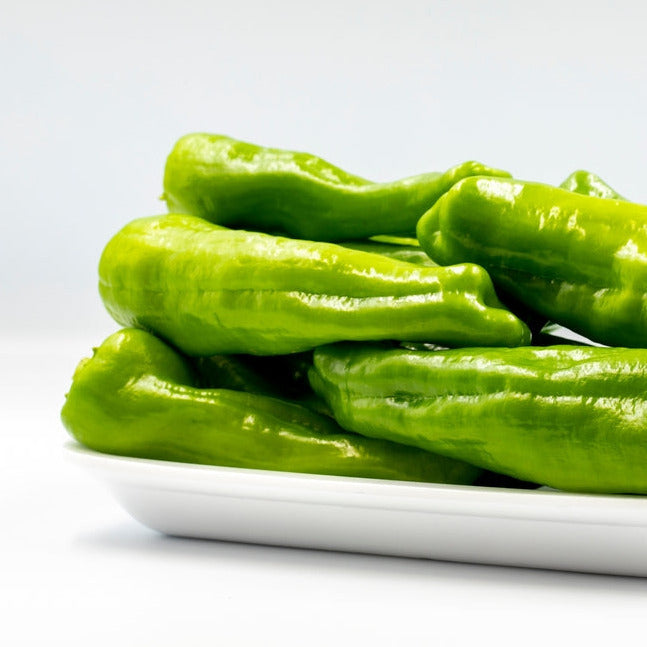 A group of fresh green Cubanelle peppers placed on a white plate against a white background.