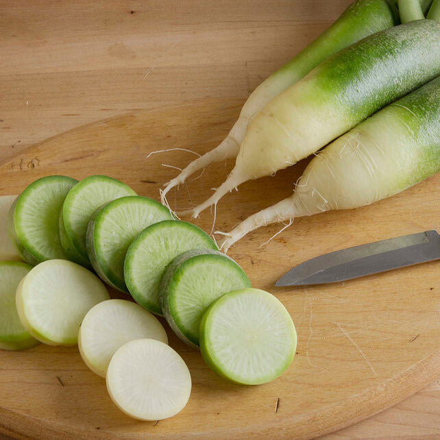 A group of green radish bulbs on a wooden cutting board with a knife, indicating they are ready for cutting and cooking.
