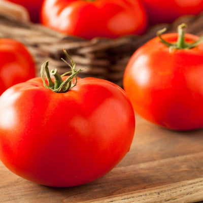 A cluster of bright red, ripe tomatoes with a green stem, placed on a wooden surface.