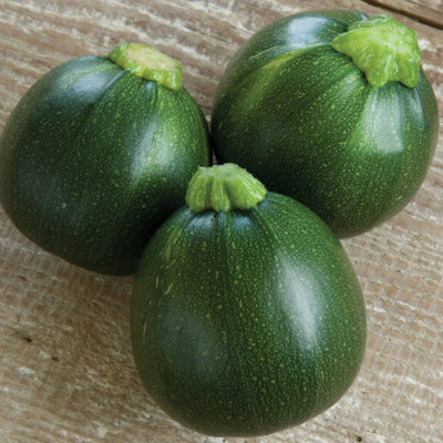 Three round, dark-green zucchini placed on a wooden surface.