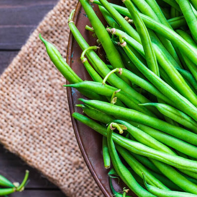 A bunch of fresh green beans on a brown background, with a few beans placed on a burlap mat beside the bowl.