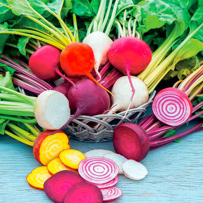 A variety of beetroot sliced and whole, with greens and radish-colored ends, arranged in a basket.
