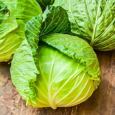 A group of fresh green cabbage heads with leaves, placed on a wooden surface.