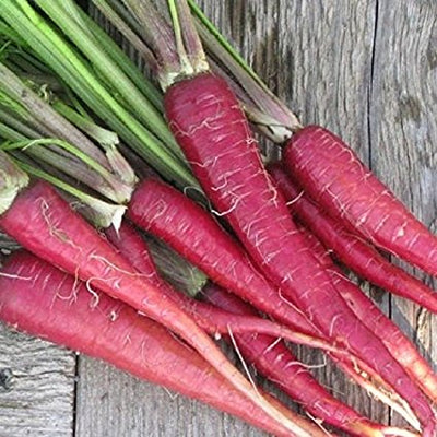 A group of Atomic Red carrots with green tops, laid out on a wooden surface.