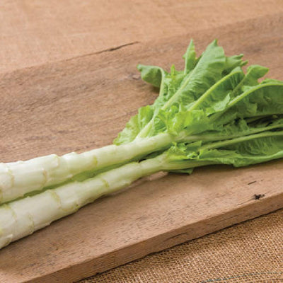 A fresh celtuce stem with green leaves resting on a wooden surface.