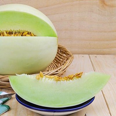 A green honeydew melon cut open to show the seeds and flesh, placed on a wooden surface.