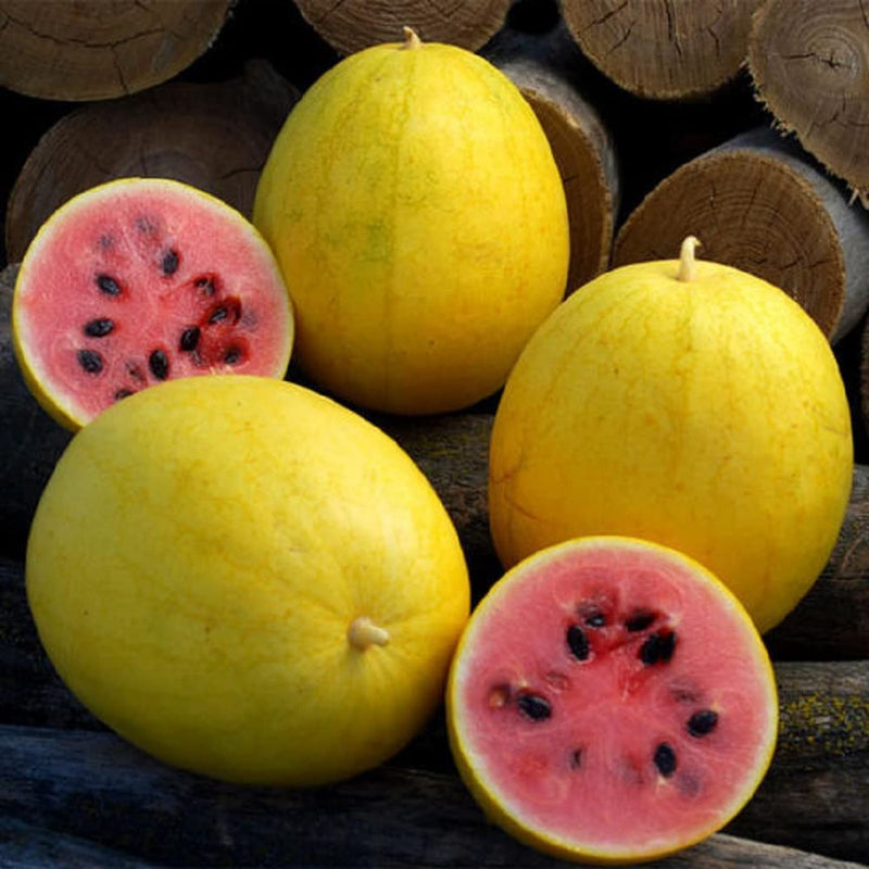 Three Golden Midget watermelons, one whole and two sliced in half, displaying the red flesh and black seeds, placed on a surface with wooden elements in the background.
