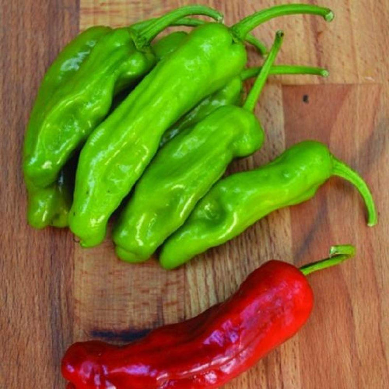 A group of three green pepperoncini peppers on a wooden surface, with one pepper turning red at the bottom.