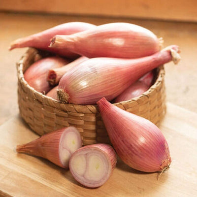 A basket filled with elongated bulbs of Shallot Creme Brulee, with a few sliced in half to show the interior, on a wooden surface with a blurred background.