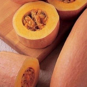 A photo showing pink-skinned winter squash cut open to reveal the seeds inside, on a wooden surface.