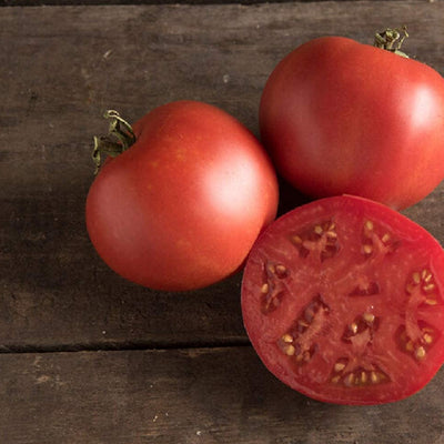 Two whole tomatoes and one half-cut tomato on a wooden surface, showcasing the deep red color and internal structure.