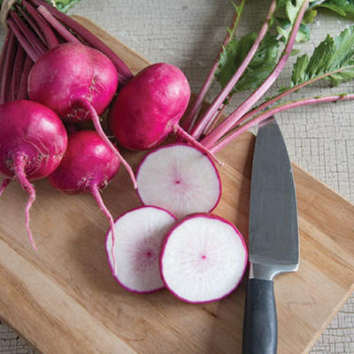 A group of red-stemmed turnips with white flesh, alongside a knife on a wooden cutting board.